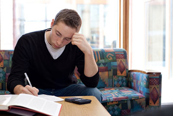 A male student completing his math assignments with an opened textbook and a calculator; Shutterstock.com