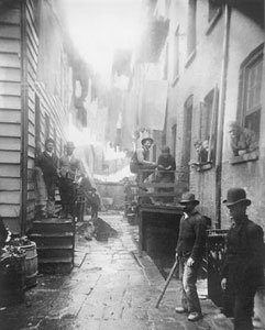 narrow city street with men in bowler hats standing along the sidewalk