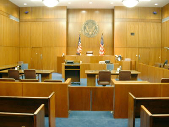 empty courtroom showing judge’s bench, jury box, witness stand, and prosecution and defense tables
