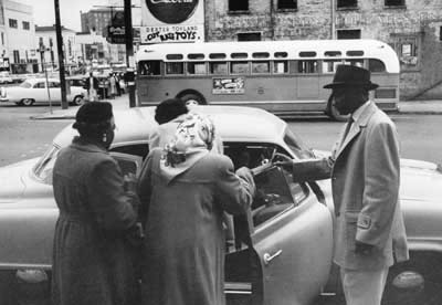 African Americans entering a car; an empty bus is in the background