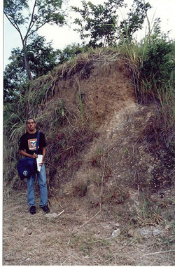 a man standing beside a cliff of exposed soil