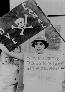 a woman from the Love Canal site holding a sign that says "We've got better things to do than sit around and be contaminated."