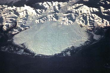 A glacier at the bottom of a mountain. The glacier forms a wide lobe at the foot of the mountain.