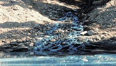 a blue liquid running into and polluting a stream