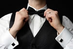 A man in a tuxedo tying his bow tie.