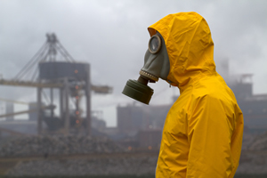 Man wearing gas mask standing infront of factory. 