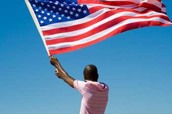 A person waving the American flag against a blue sky; Shutterstock.com