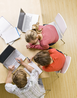 Three students using laptops and collaborating together at a table