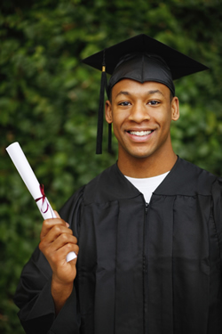 A male student wearing a graduation cap and grown and holding a diploma