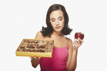 Woman deciding between a box of chocolates and an apple.